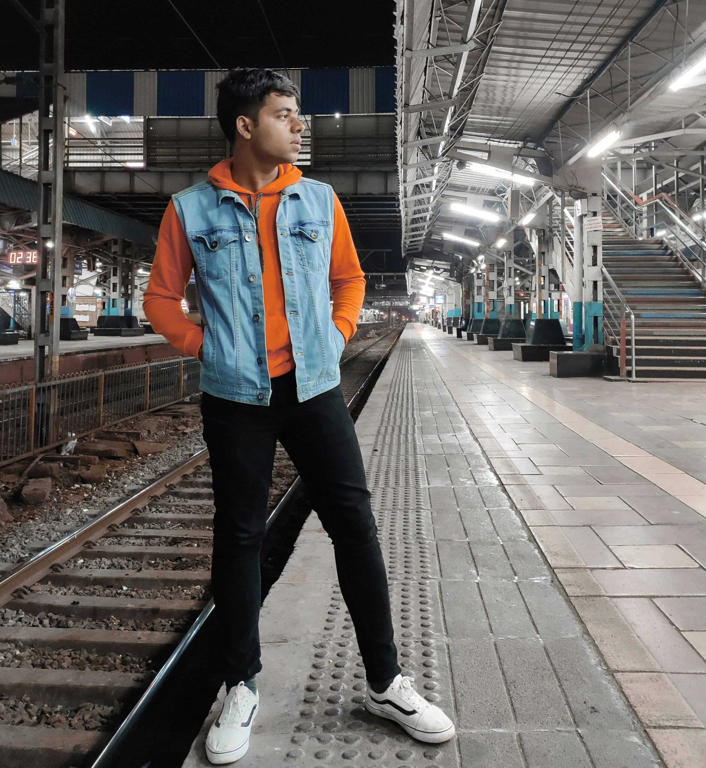 駅のホームに立つデニムベストを着た若い男性